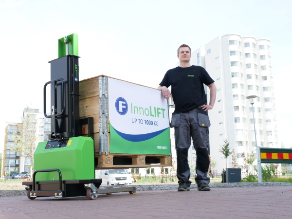 En mand, der står ved siden af en InnoLIFT-maskine og dens last og foran en hvid lejlighedsbygning.
